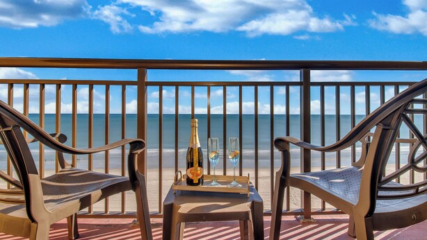 A balcony with two chairs, a table, and a bottle of champagne. - Romantic Oceanfront 1-Br w/ Balcony (Myrtle Beach)