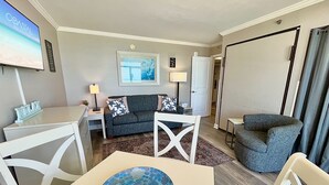 A living room with a sofa, a dining table with a decorative plate, a TV, and a door. - Romantic Oceanfront 1-Br w/ Balcony (Myrtle Beach)