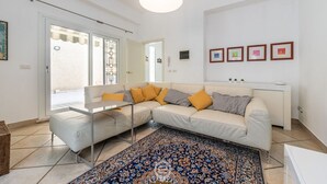 Ein modernes Wohnzimmer mit einem beigefarbenen Ecksofa, einem Glastisch, einem gemusterten Teppich und einem weißen Konsolentisch mit gerahmten Bildern.
