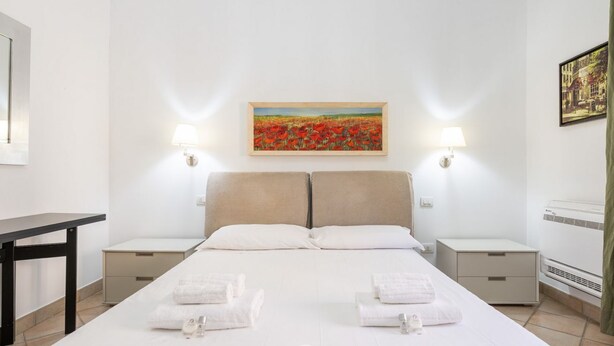 Ein Hotelzimmer mit einem großen Bett, zwei Nachttischen, einem Schreibtisch und einem Gemälde an der Wand.