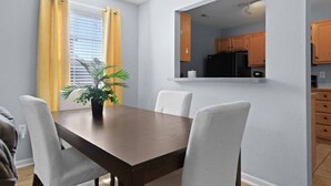A dining area with a wooden table and white chairs, a potted plant, and a view of a kitchen with wooden cabinets and a black refrigerator. - New! Spacious 4 Bed Great for Commuting, Dogs ok (Columbia)