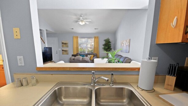 A modern kitchen with a double sink, a ceiling fan, and a view into the living area through a large mirror. - New! Spacious 4 Bed Great for Commuting, Dogs ok (Columbia)