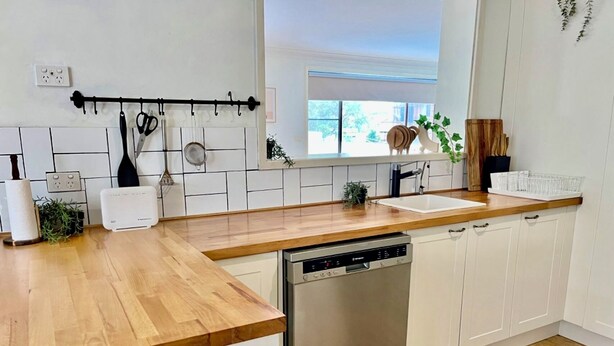 A modern kitchen with a wooden countertop, white cabinets, a dishwasher, and a window with a view of greenery outside.