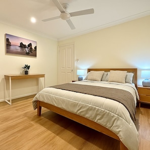 A bedroom with a bed, bedside tables, a ceiling fan, a wall-mounted TV, and a door. - Festive Coastal Retreat - Private Pool (Nowra)