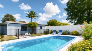 A swimming pool with a blue edge, surrounded by a fence, and two lounge chairs.