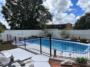 A backyard with a swimming pool, a white fence, and a house in the background. - Festive Coastal Retreat - Private Pool (Nowra)