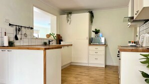A modern kitchen with white cabinets, a wooden countertop, and a central island. There is a microwave on the countertop, and a plant is placed on top of the cabinets.