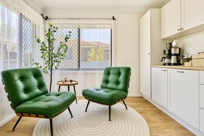 A modern living room with two green leather armchairs, a small round table, and a view of the outside through a window with a white curtain.