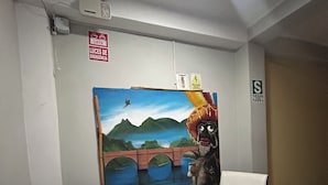 A room with two white chairs, a small white table, and a mural on the wall depicting a landscape with mountains and a bridge. - Hotel Paraíso L&M (Huánuco)