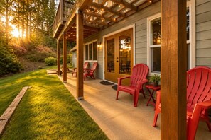 A covered patio with red Adirondack chairs, a wooden deck, and a house with a glass door. - Hot Tub I Peloton I Ping Pong I Dogs OK (Clinton)
