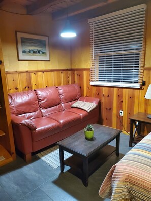 A cozy room with a red leather sofa, a small wooden coffee table with a potted plant, a window with blinds, and a framed picture on the wall. - Comfy, homey studio with private entrance and snack-prep area (Long Beach)