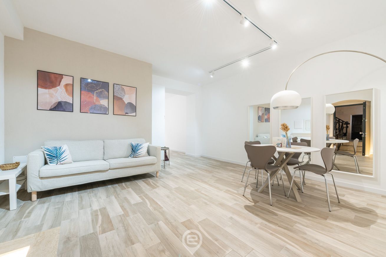 Uma sala de estar moderna com um sofá branco, uma mesa de jantar com cadeiras e arte abstrata nas paredes.