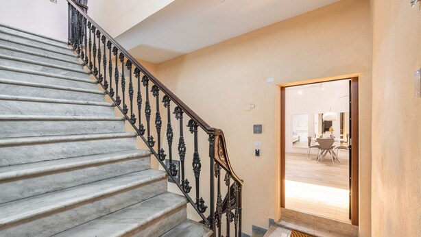 A marble staircase with ornate black railings leading to a room with a wooden floor and a door leading to a dining area. - Sofia House - City Centre (Cagliari)