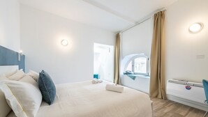 A modern hotel room with a large bed, a window with curtains, a radiator, and a desk with a chair. - Sofia House - City Centre (Cagliari)