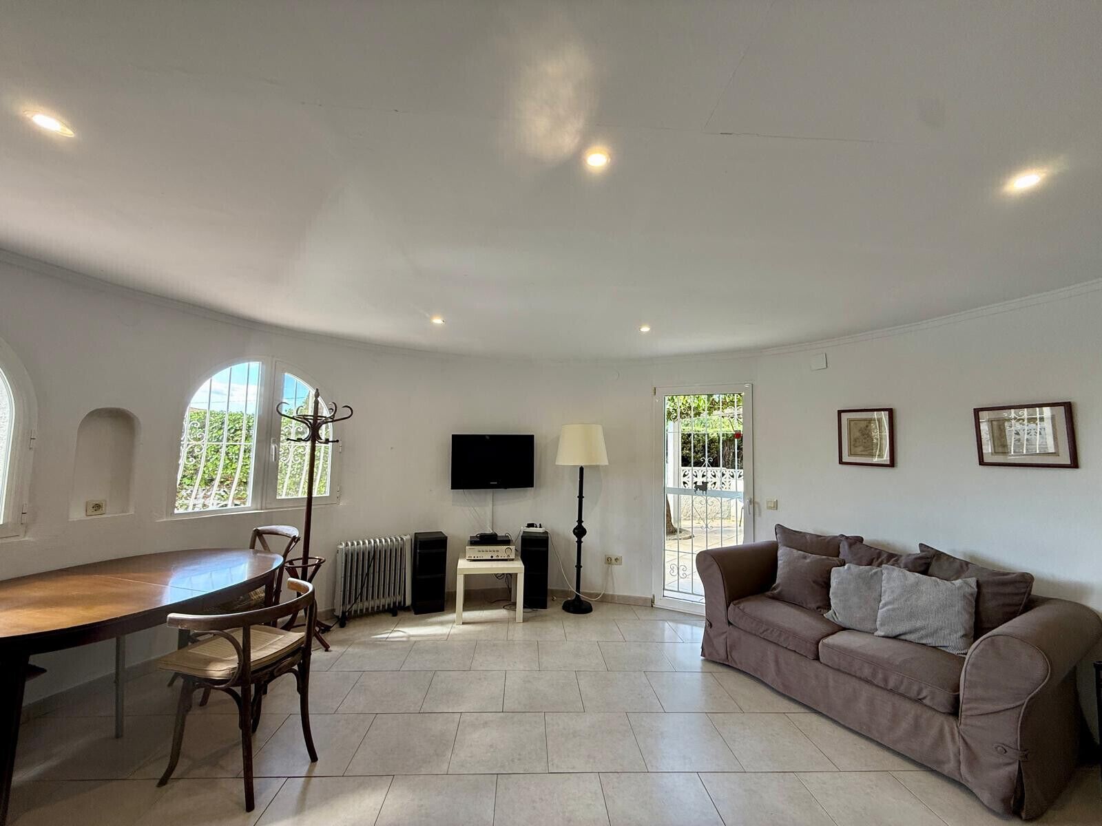 A spacious living room with a dining table, chairs, a sofa, a TV, and a radiator.