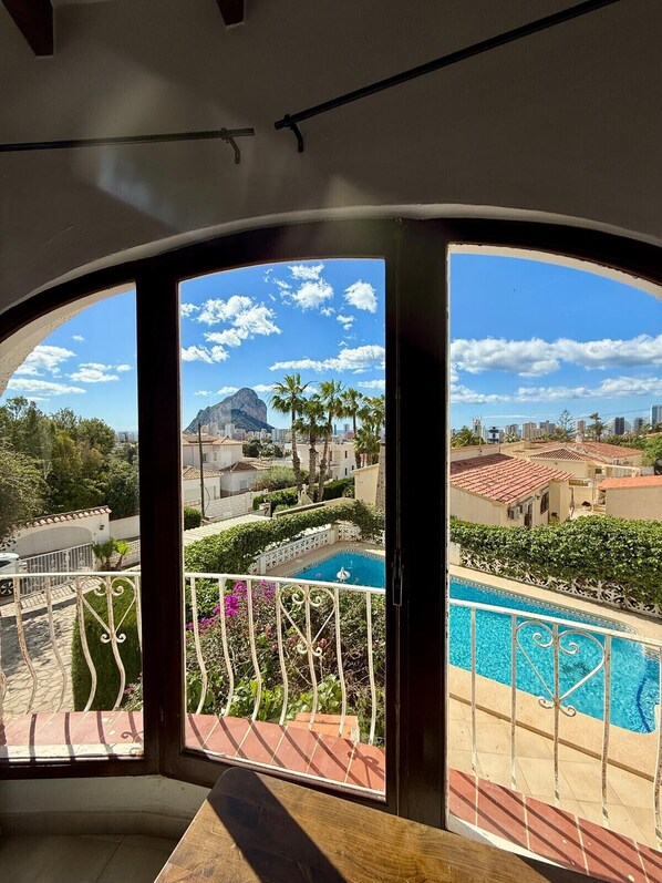 A view from a balcony with a pool, a mountain, and a cityscape.