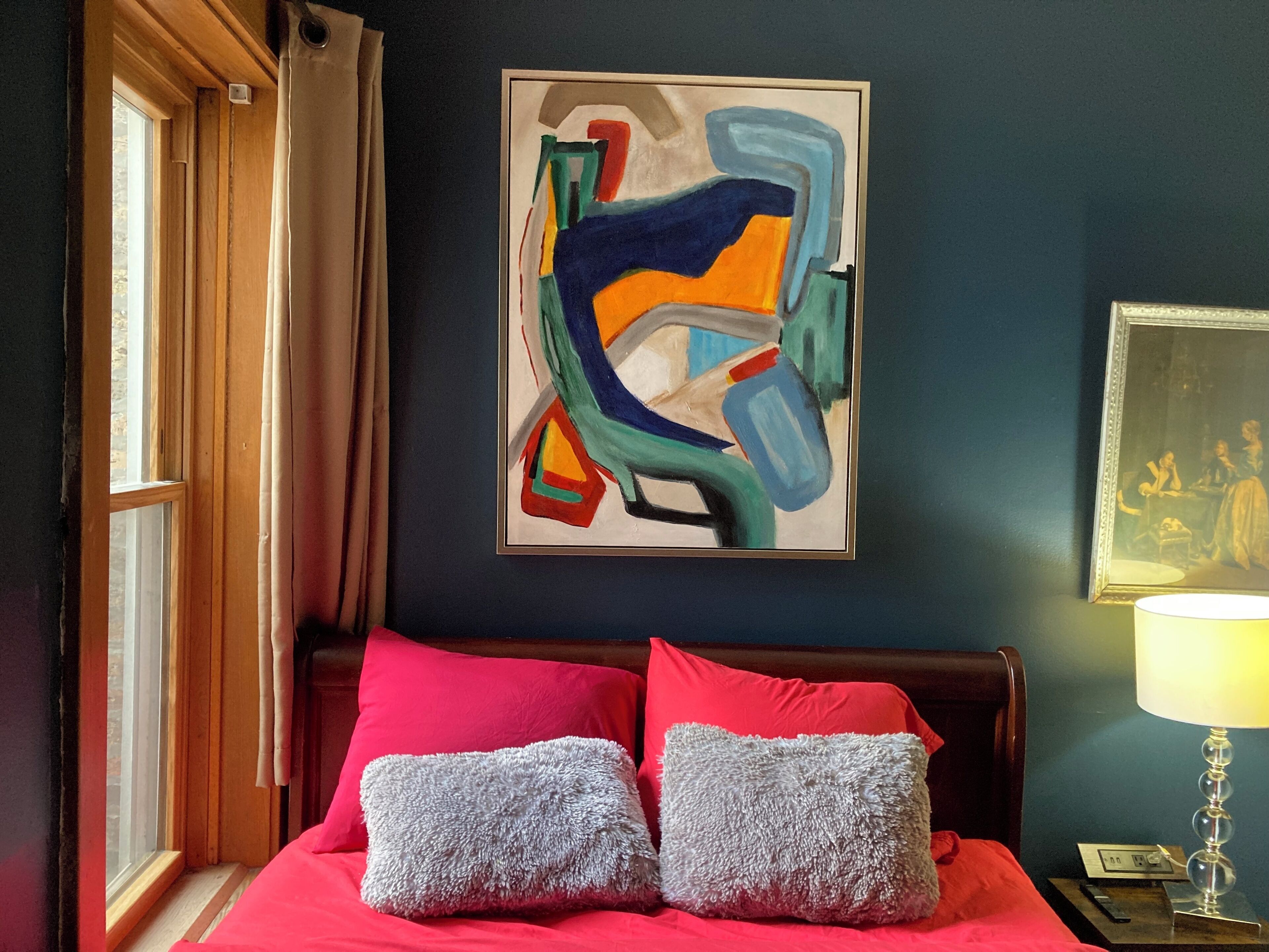 A bedroom with a bed, two pillows, a painting, a lamp, and a window.