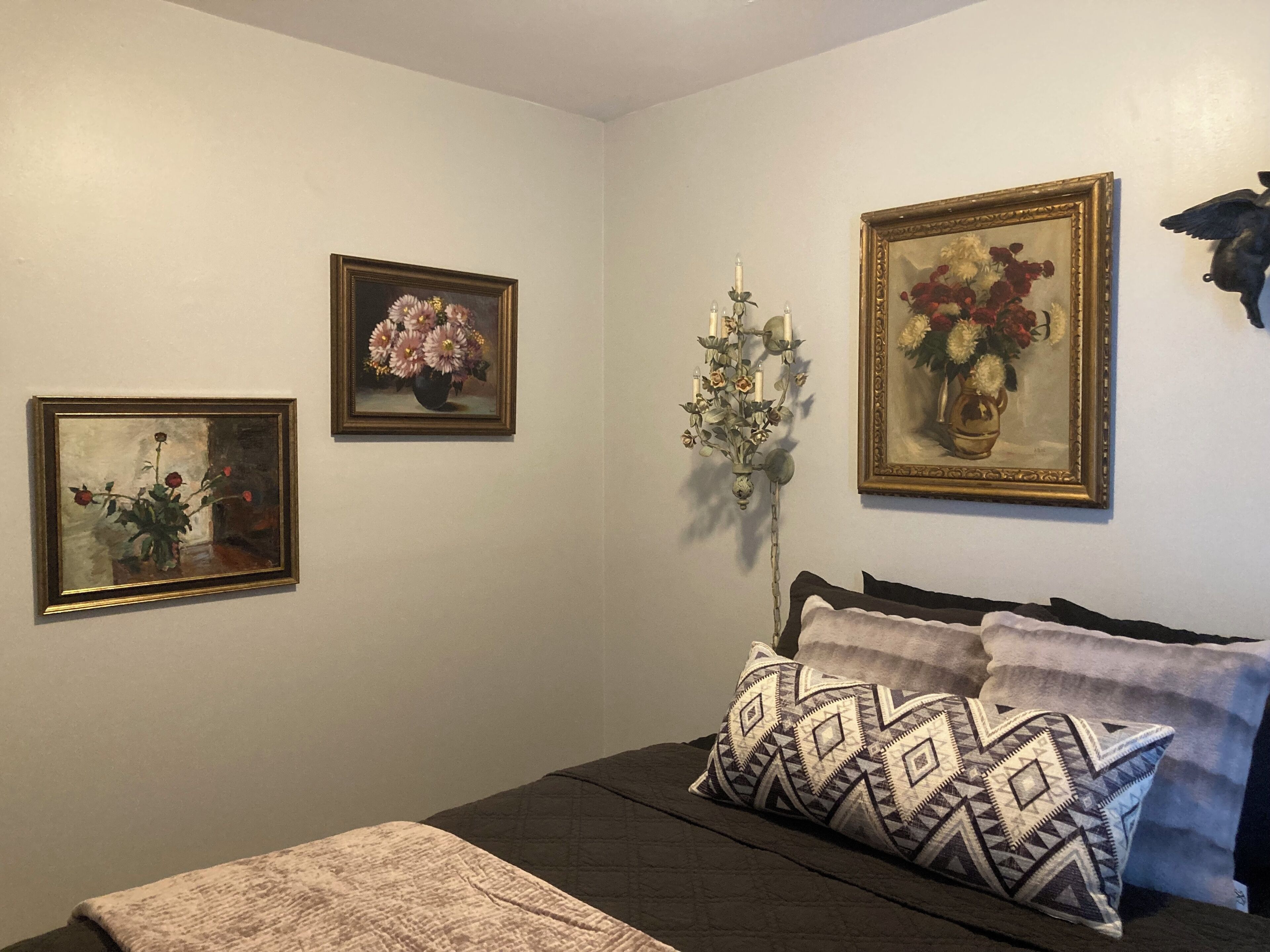 A bedroom with a bed, pillows, and three framed floral paintings on the wall.