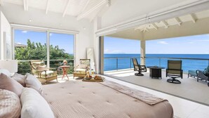 Ein geräumiges Schlafzimmer mit einem großen Bett, einem Balkon mit Sitzgelegenheit und Blick auf den Ozean.