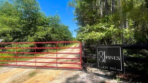 A gated entrance with a sign reading "81 Pines EST. 2022" and a dirt road leading into a wooded area. - 81 Pines-The Cabin (Waycross)