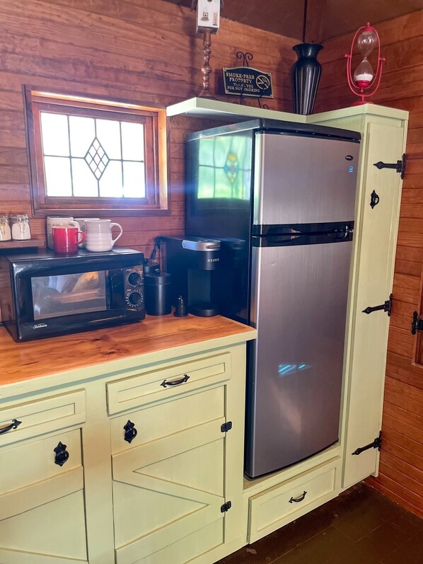 A kitchenette with a stainless steel refrigerator, a microwave, and a coffee maker on a wooden countertop. - 81 Pines-The Cabin (Waycross)
