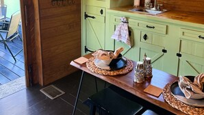 A rustic kitchen with a green cabinet, wooden walls, and a window with a stained glass design. - 81 Pines-The Cabin (Waycross)