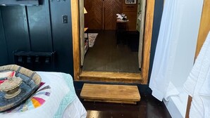 A room with a bed, a television, a wooden ceiling, and a door leading to another room. - 81 Pines-The Cabin (Waycross)