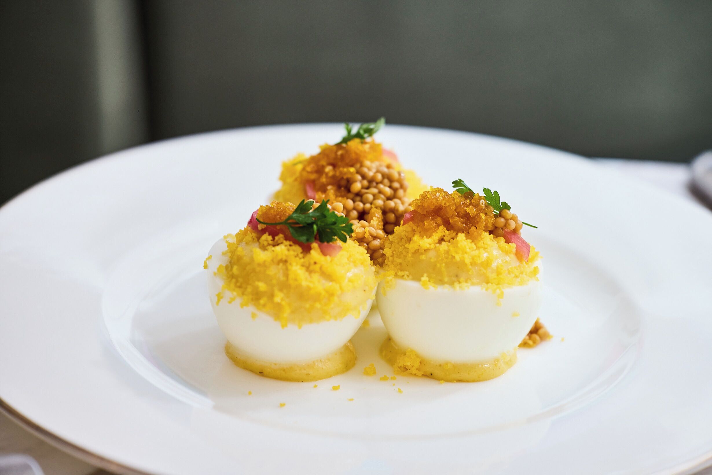 A white plate with three deviled eggs garnished with yellow crumbs and parsley.