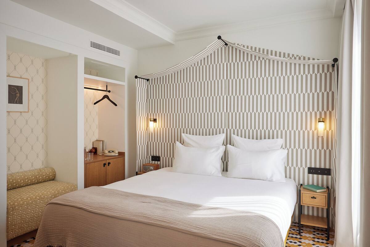 A neatly arranged bedroom with a bed, bedside tables, a wardrobe, and a hanging coat rack.