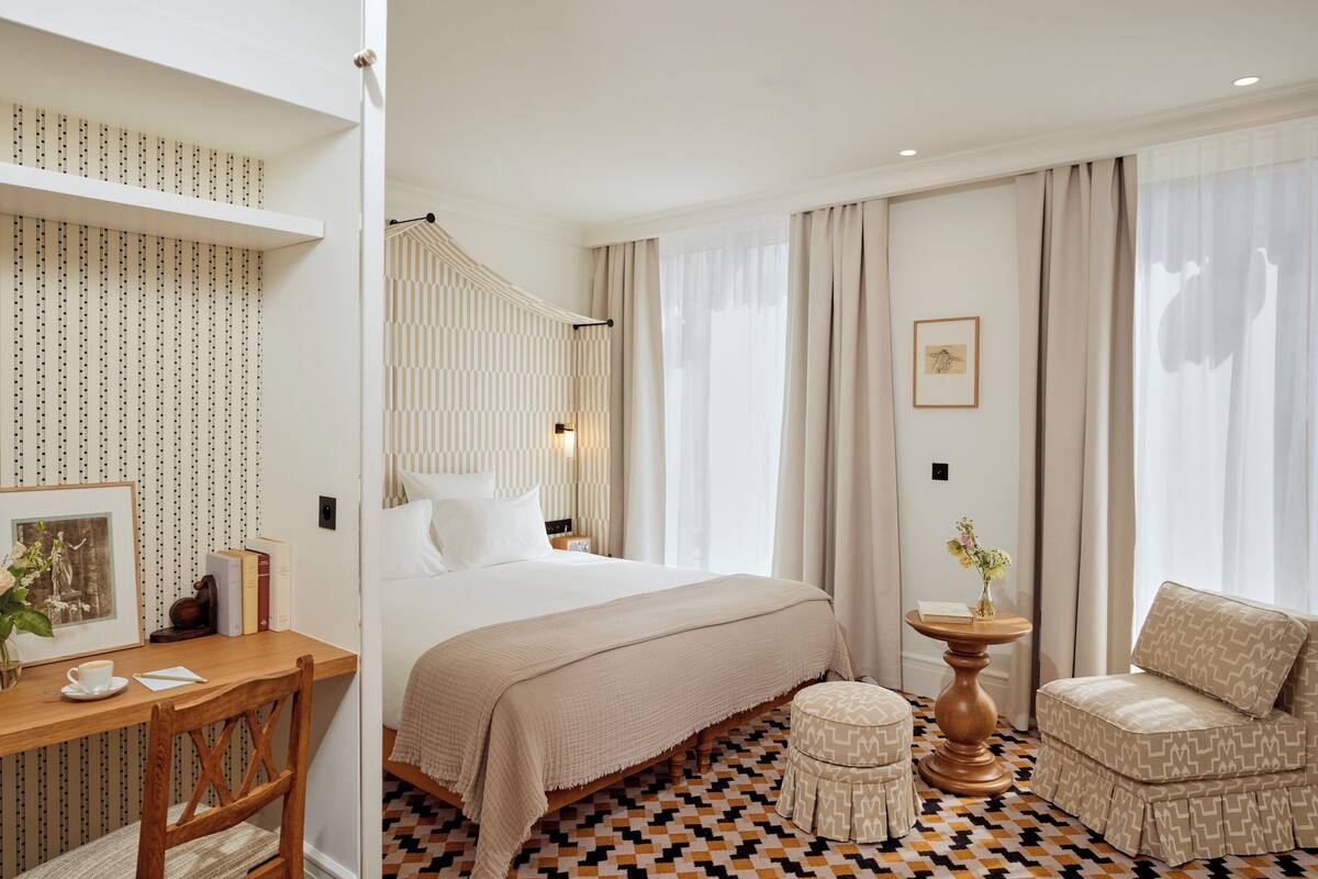 A hotel room with a large bed, a wooden desk, a patterned armchair, and a patterned floor.