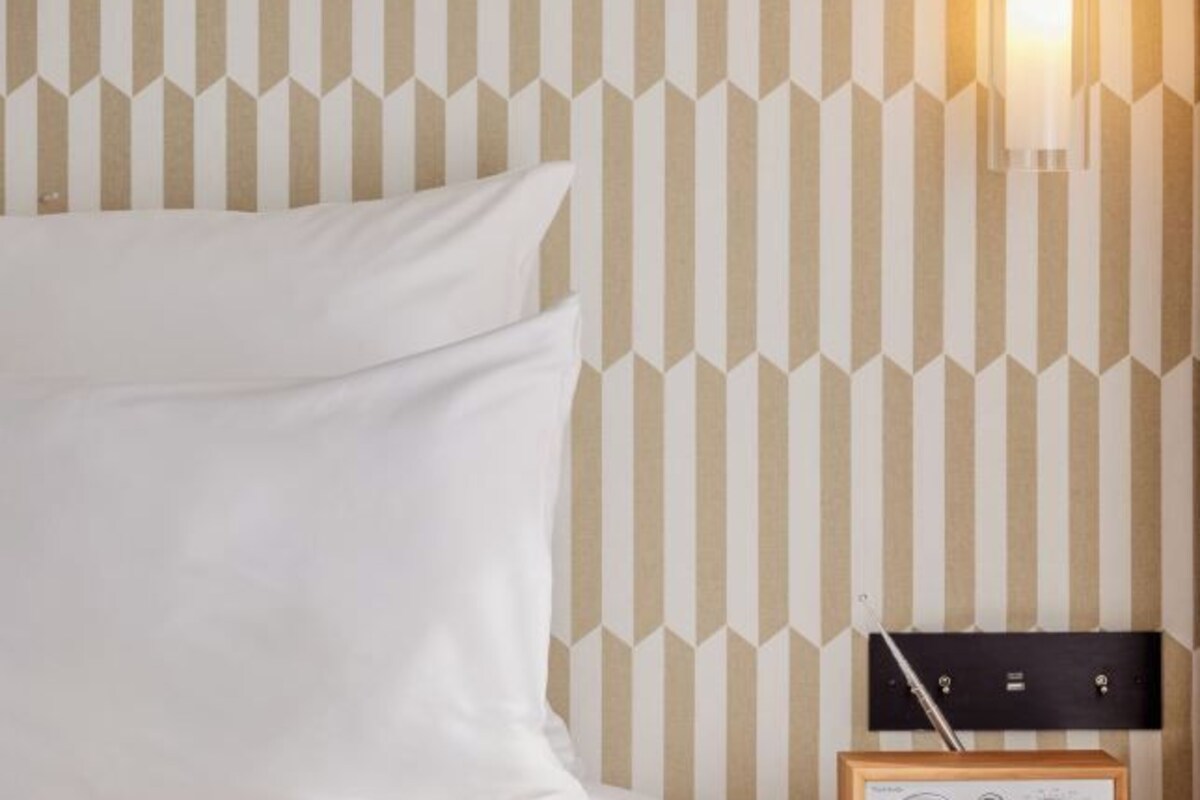 Une chambre d’hôtel avec un lit, une table de chevet avec une lampe et un mur orné d’un motif géométrique.