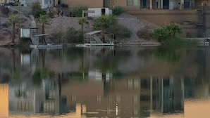 Una zona residencial moderna con edificios de varios pisos, una masa de agua tranquila que refleja las construcciones y un pequeño embarcadero con escalones que bajan al agua.