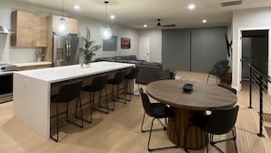 Una cocina moderna con una isla central, taburetes negros y una mesa de comedor con sillas.