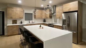 Una cocina moderna con una isla grande, electrodomésticos de acero inoxidable e iluminación colgante.
