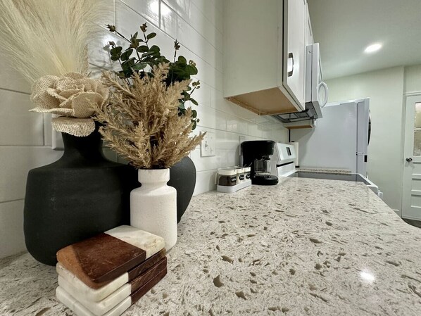 A kitchen with a granite countertop, a coffee machine, and a white refrigerator.