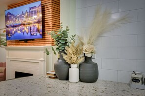 A kitchen counter with three vases containing plants and a decorative item, a television mounted on a wooden wall, and a tiled backsplash.