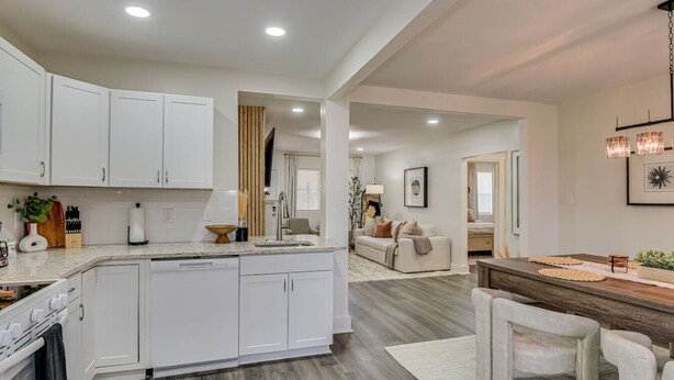 A modern kitchen with white cabinetry, a central island, and a dining area with a wooden table and chairs. - Organic Modern Apt: 1mi to Masters with Pool Table (Augusta)
