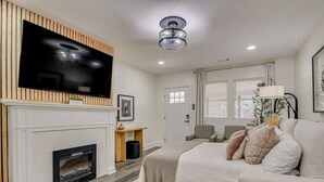 A modern living room with a flat-screen TV mounted on a wooden wall, a fireplace, a sofa with cushions, and a ceiling fan. - Organic Modern Apt: 1mi to Masters with Pool Table (Augusta)