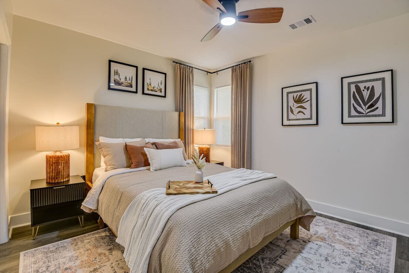 A bedroom with a bed, two bedside tables, a ceiling fan, and framed artwork on the walls.
