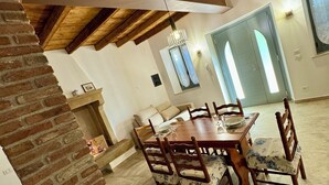 Una àmplia zona de dinar amb taula i cadires de fusta, paret de maó i alt sostre amb bigues al descobert.