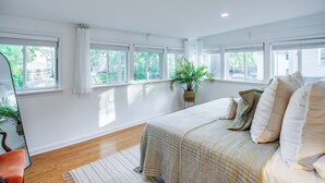 A bedroom with a large bed, multiple windows, a potted plant, and a mirror.