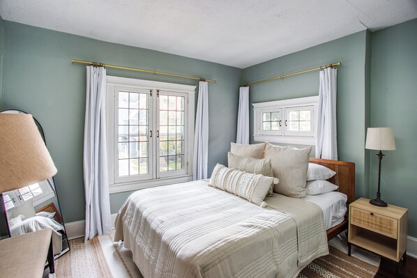 Un dormitorio con cama, mesitas de noche, lámpara y ventana con cortinas.