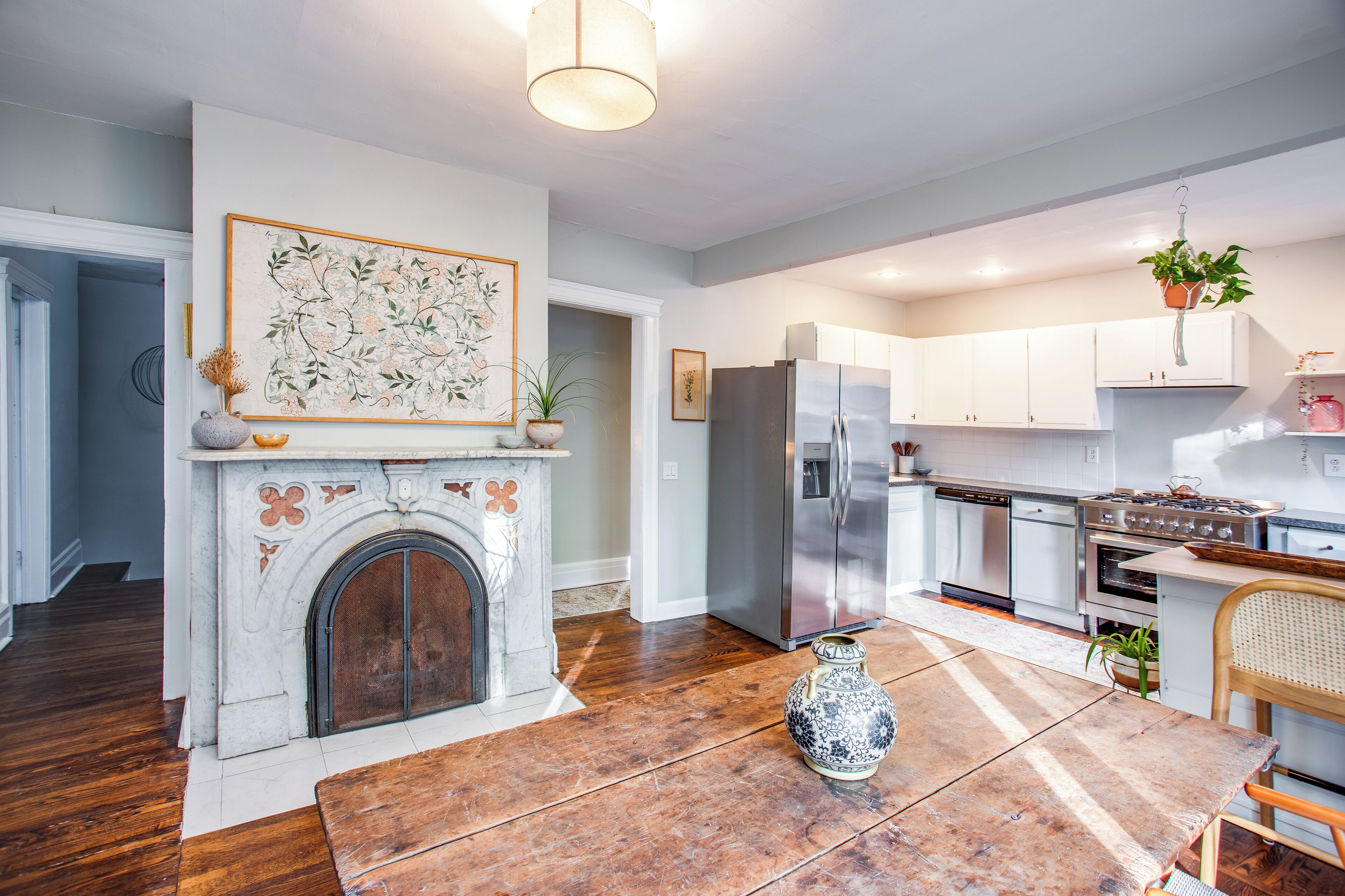 A modern kitchen with white cabinets, a stainless steel refrigerator, and a fireplace with a decorative vase.