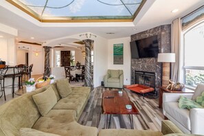 A modern living room with a sectional sofa, a fireplace, and a dining area in the background. - Mountain View Oasis  AC, Pool, Pet & Family Friendly (Hemet)