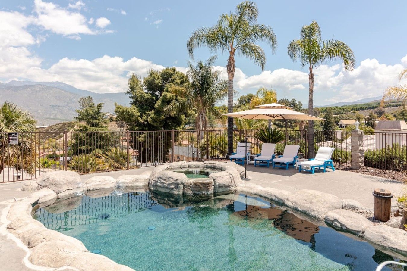 A swimming pool with lounge chairs and palm trees, surrounded by a fence.
