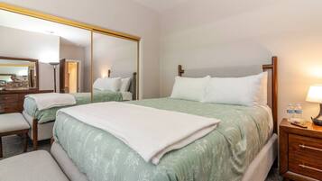 A hotel room with a large bed, a bedside table with a lamp, a mirror, and a small desk with a chair.