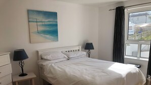 Ein ordentlich bezogenes Bett mit weißen Leinen, zwei Nachttischlampen, ein kleiner Nachttisch und ein Meeresbild an der Wand.