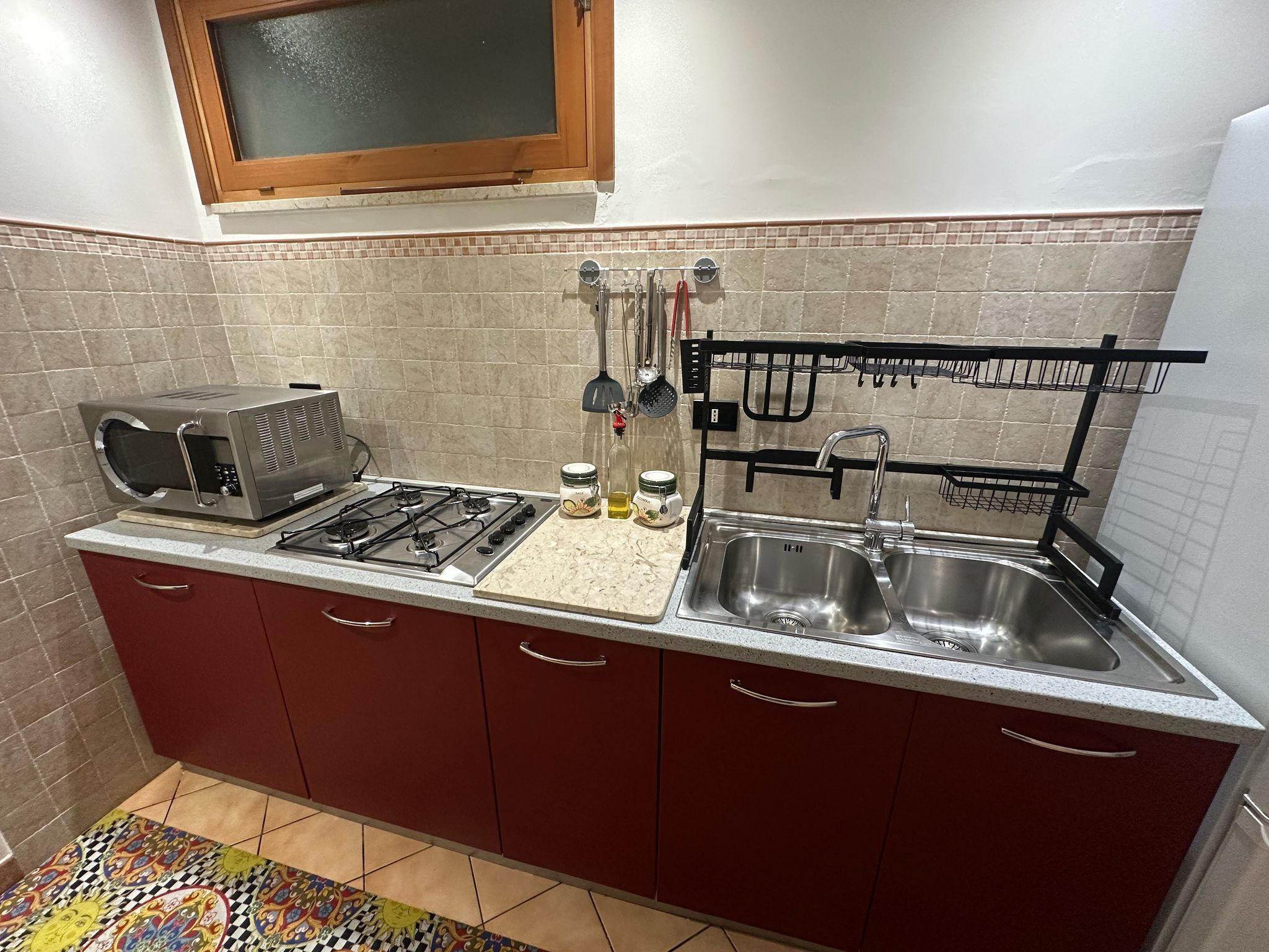 Una cucina compatta con piano cottura a gas, forno a microonde, lavello a due vasche e finestra sopra il lavello.