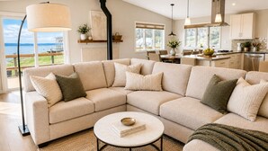 A modern living room with a sectional sofa, a round coffee table, and a view of the outdoors. - Hot Tub by the Water | Sunset Deck | Beach Access (Greenbank)