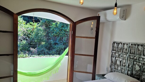 A bedroom with a bed, a hammock, and a view of greenery outside.